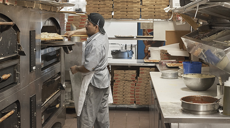 Pizzaiolo putting pizza in deck oven