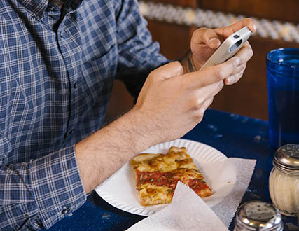 Man using phone while eating a slice of pizza